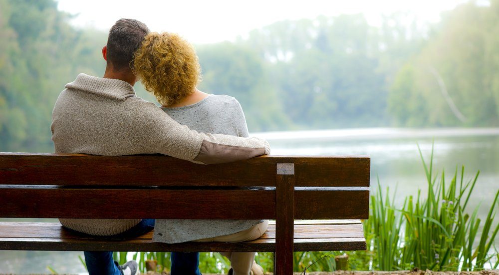 Two people sitting together on a bench looking out over a lake